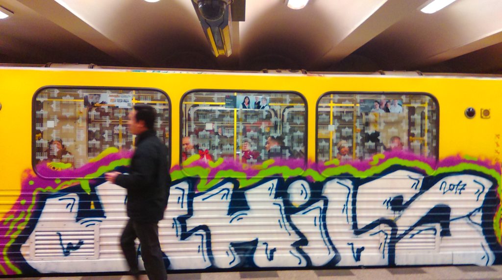 A person walks by the UCHILS Graffiti Bombing on the yellow panel of the Berlin Metro.