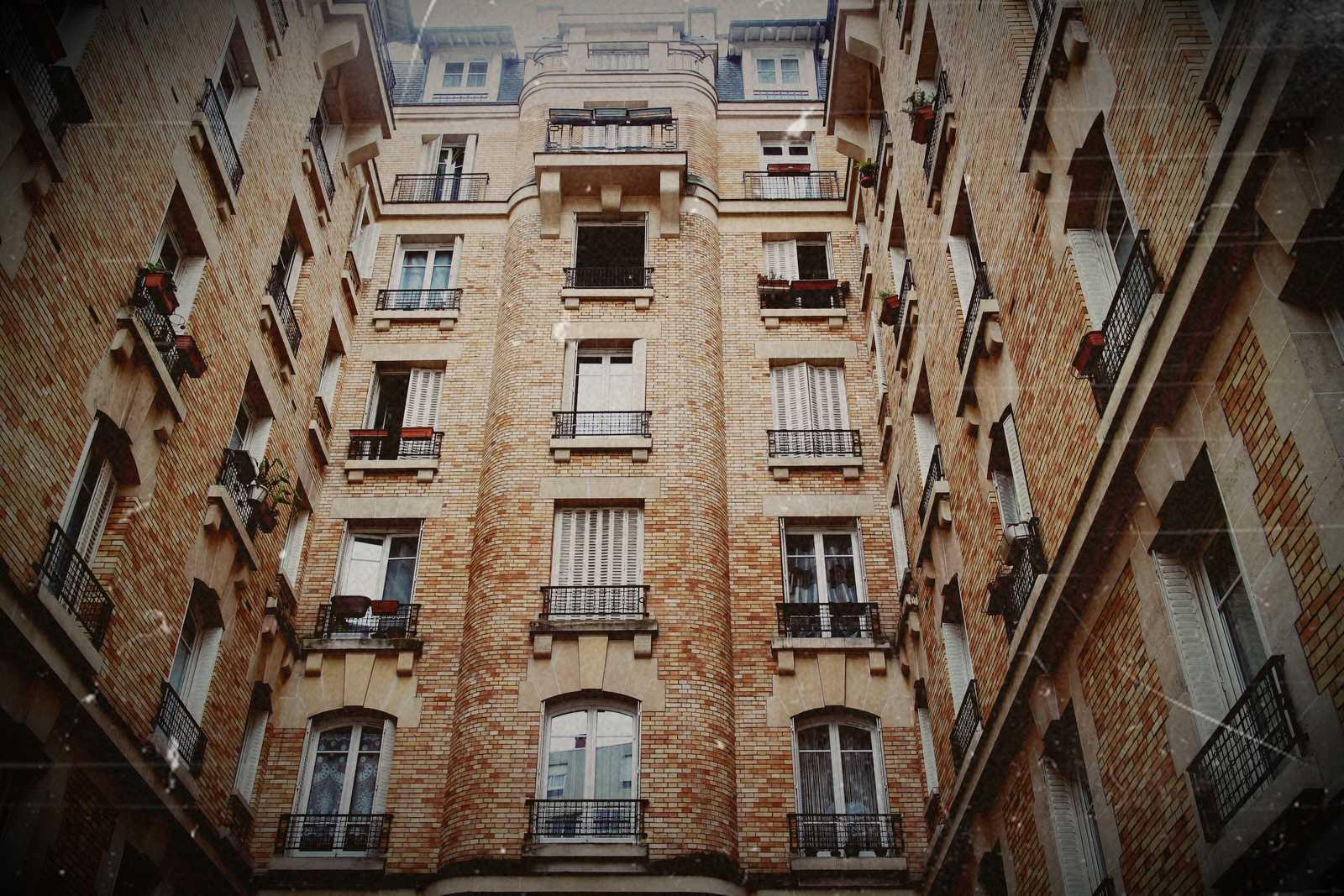 Caption of a courtyard in the neighboorhood of "Batignolles" in the 17th Arrondissement. The building is made of orange bricks and is quite dense. More then 6 storeys high the three buildings are filling the entire image.