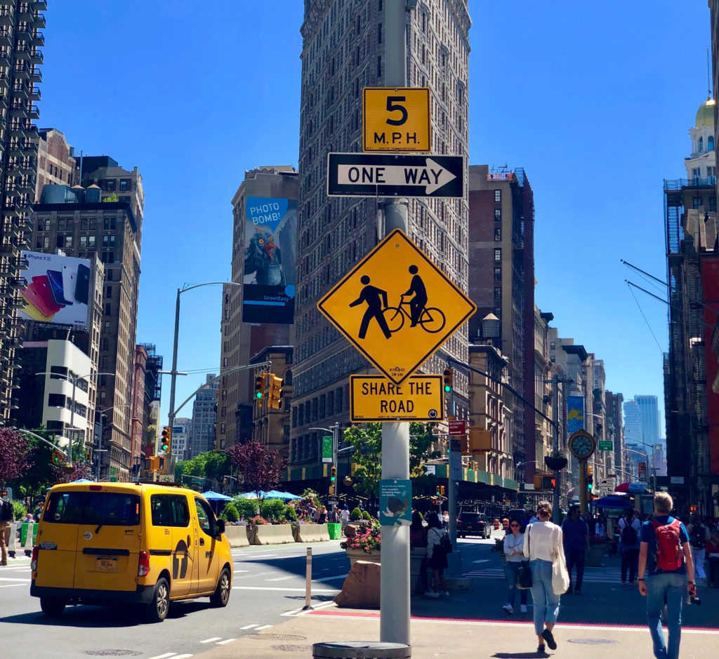 Erfolgsgeschichte taktische Urbanismus, Broadway New York, Wolkenkratzer, Fußgängerzone, autofrei, Autoverkehr, Öffentlicher Raum, Stadtleben, Passanten, Gelbes auto. Shild "Share the Road", taktischer Urbanismus