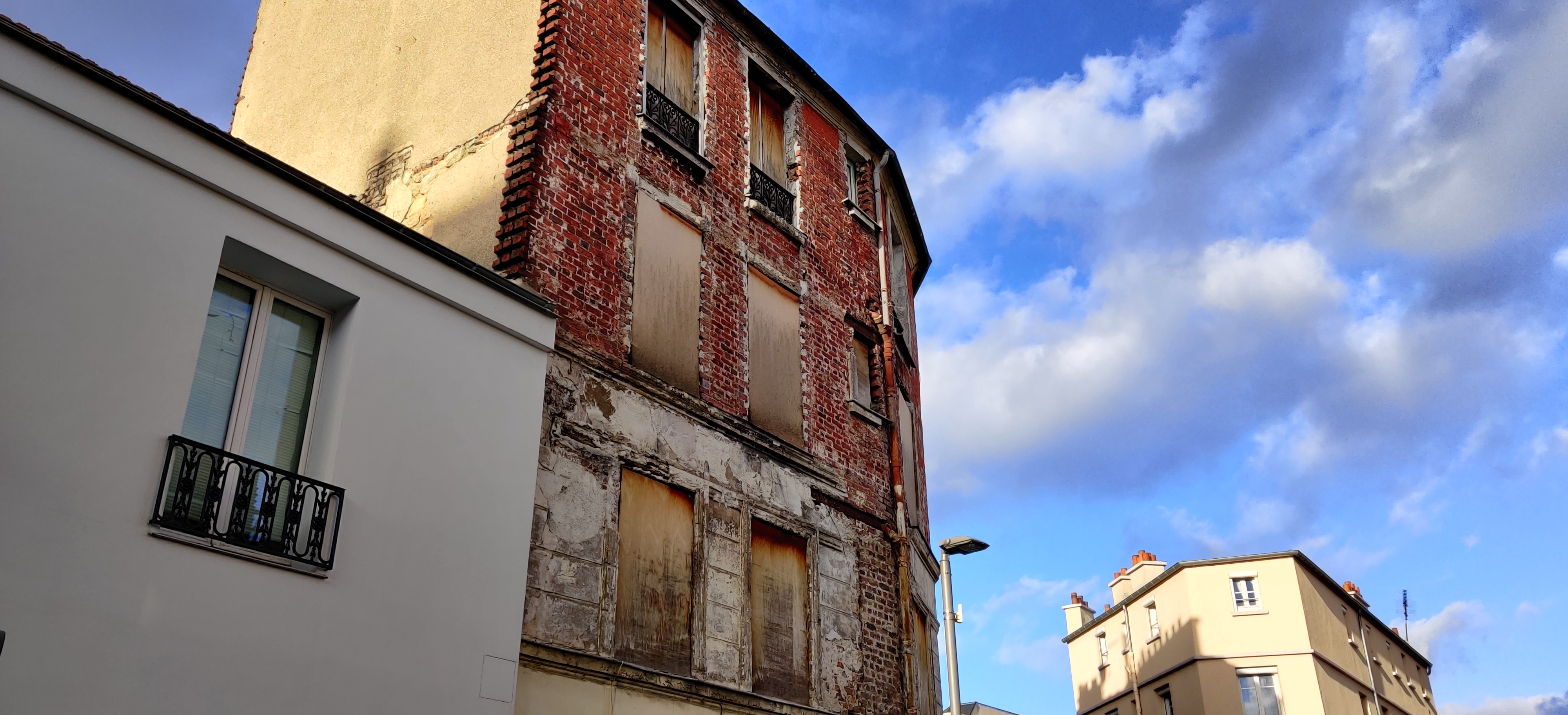 verbarriakdiertes Haus. Holzplatten vor den Fesntern, Rotes Backsteinhaus, Banlieue Vorort von Paris, Himmel blau, leicht bewölkt, belichtung nachmittags