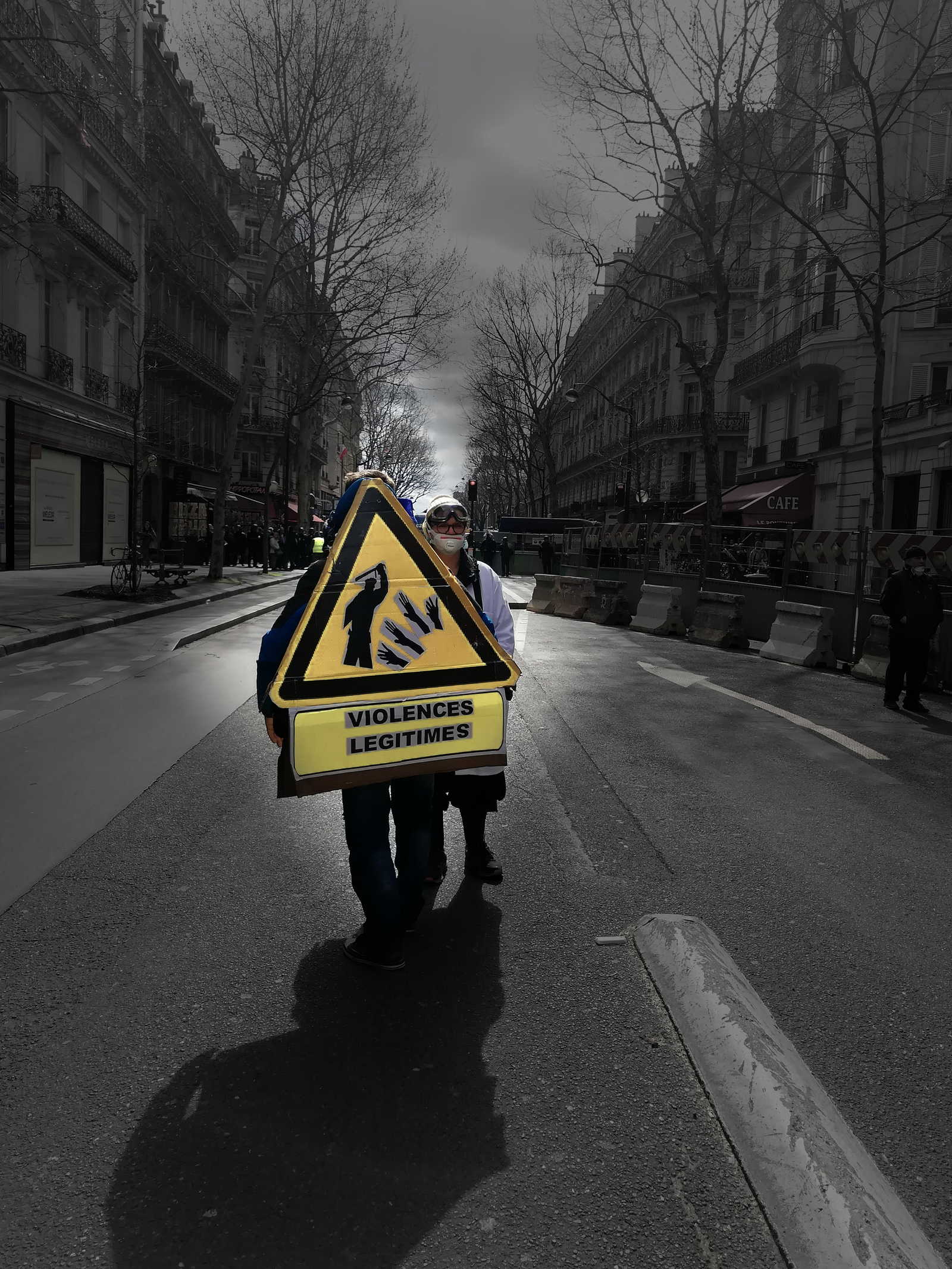 Two protesters of the Yellow Vest mouvement are standing on a street in Paris near the Champs-Elysee. one of the demonstrators is wearing a costume in the form of a warning sign that says: "Legit Violence", while a dark silhouette can be seen beating on hands on the sign. .