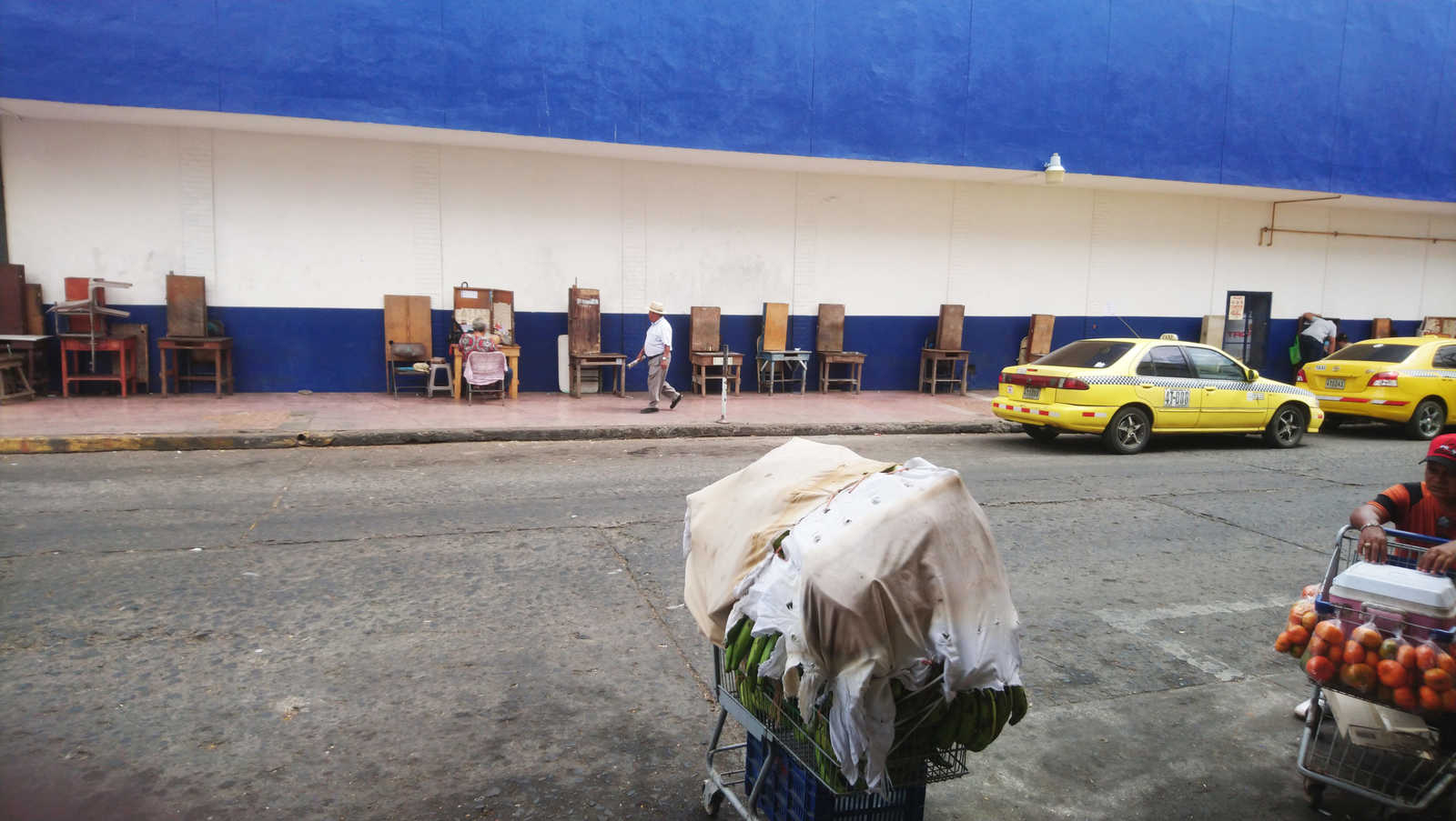 A man is walking down the pavement, while a yellow cab passes him.