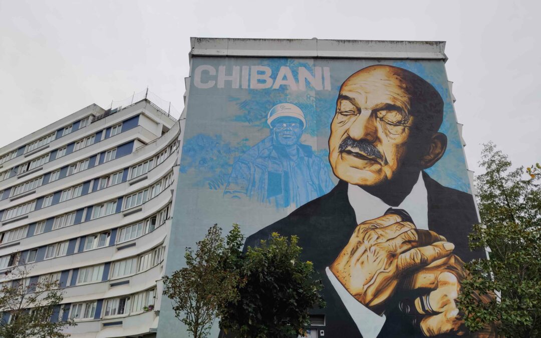 Urban art mural in tribute to chibani, a human rights activist and political person. Streetart Portrait on building: old man in a black suit, his hands holding his tie,, blue background, Location of the artwork in the public space of the Paris suburb Malakoff.