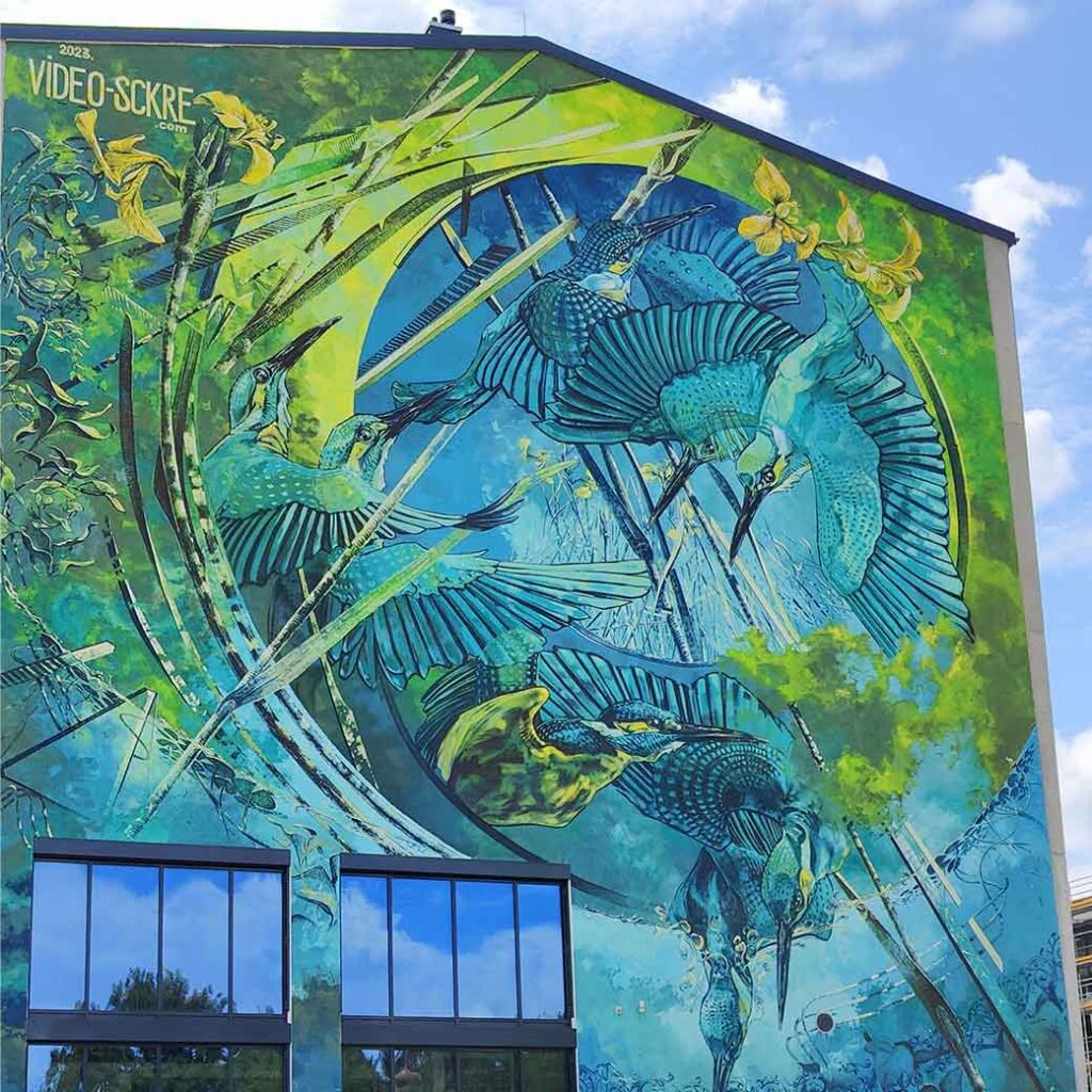 Mural by VIDEO.SCKRE in Landsberg, Bavaria, Germany. It depicts flying kingfishers and is painted in green and blue colors.